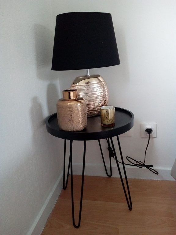 Chevet rond, lampe noire et vases cuivrés devant le mur blanc