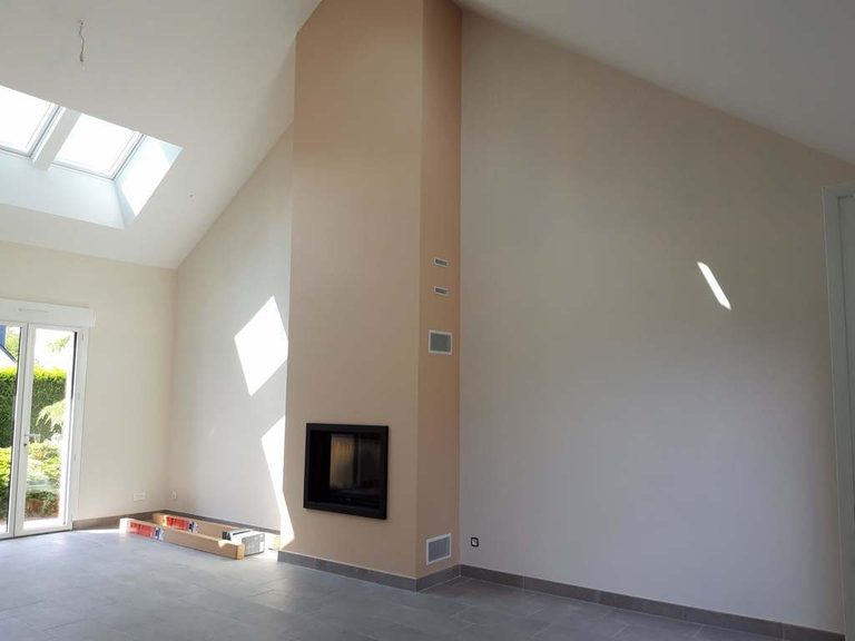 Séjour lumineux avec poêle, puits de lumière et murs beige rosé