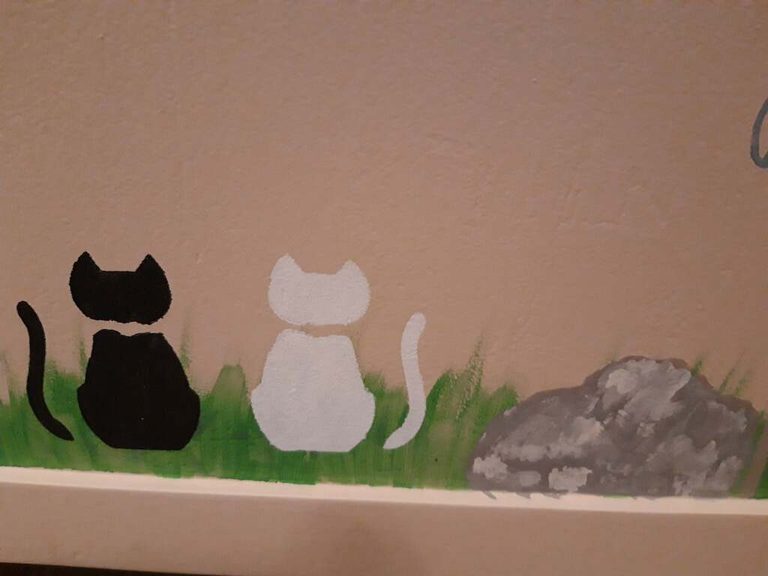 Détail du coffre : chat noir et chat blanc assis dans l'herbe près d'un rocher